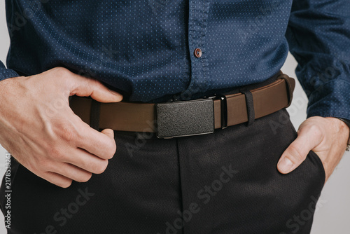 Close-up of a man wearing a brown smooth leather belt with an automatic ratchet buckle on black trousers