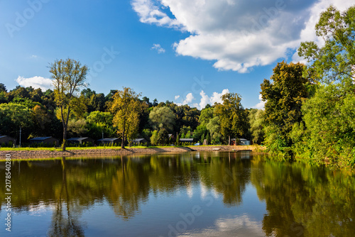 Fotografie Scenic pond reflecting lush green trees and summer blue sky near the historic St