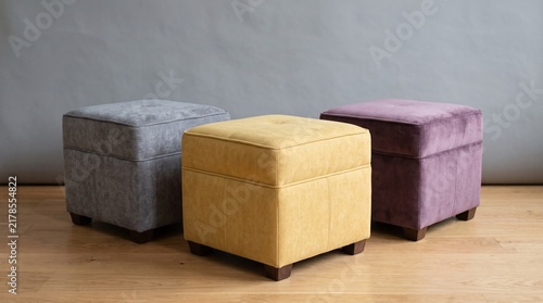 Three colorful upholstered square storage ottoman poufs on wooden floor