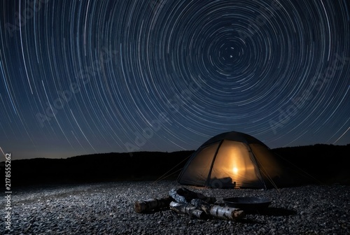 Night camping tent under star trails with warm shelter and wilderness calm