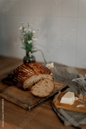 Freshly baked bread with butter on wooden table beside wildflowers in vase