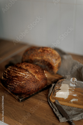 Freshly baked sourdough bread sits warm on a wooden table with butter ready to spread