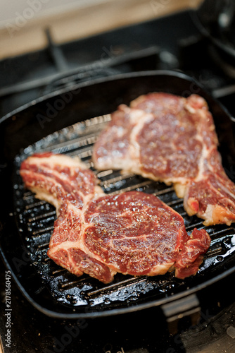 Two thick steaks sizzle on a grill pan as they cook for a delicious dinner meal at home