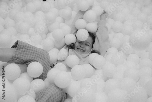 Young child laughs joyfully while playing among white balls in a ball pit at an indoor play area