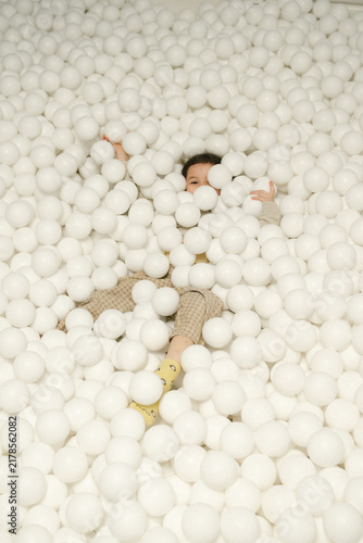 Child laughs and plays joyfully inside huge ball pit full of soft white balls