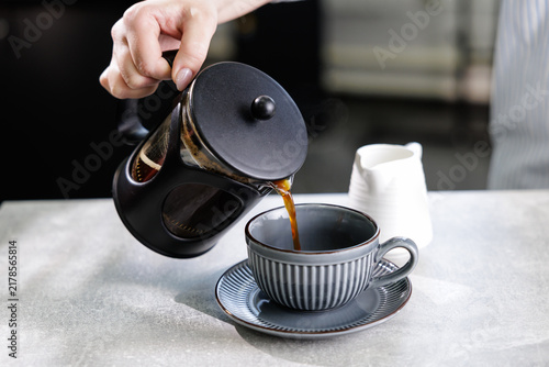 Canvastavla Hand pouring hot coffee from french press into gray striped cup and saucer for b