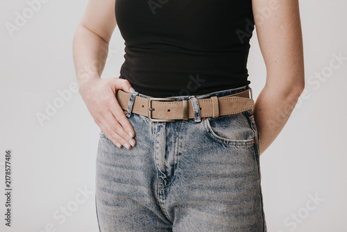 Close-up of a woman wearing a beige suede leather belt with a metal buckle on acid wash jeans