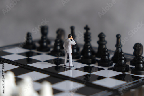 Miniature businessman standing on chessboard facing opponent pieces, business strategy, decision making, risk management, and leadership concept