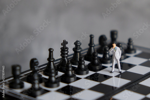 Miniature businessman standing on chessboard facing opponent pieces, business strategy, decision making, risk management, and leadership concept