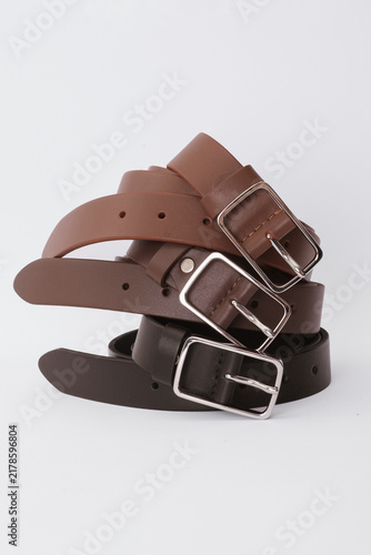 Stack of shades of brown leather belts with silver metal buckles on a white background