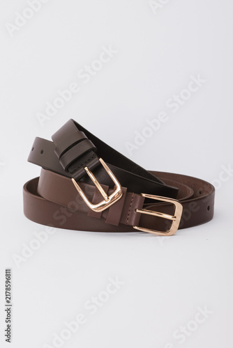Coiled brown and dark brown leather belts with gold metal buckles isolated on a white background