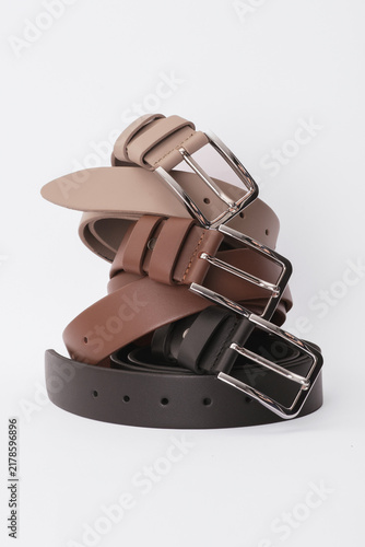 Stack of beige, brown and black leather belts with metal buckles on a white background