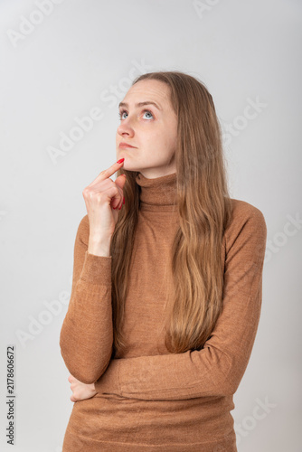 Bild auf Leinwand Young woman looking up with a thoughtful expression, holding a finger to her chi