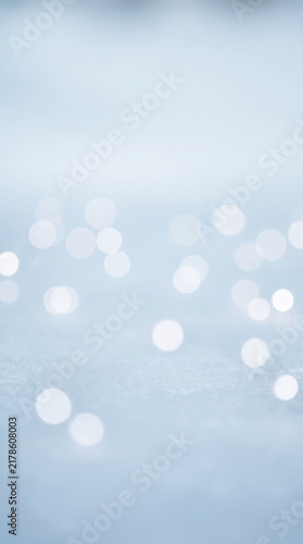 Abstract soft blue winter background with glowing white bokeh lights and sparkling snow texture for festive holiday greeting cards or elegant seasonal commercial design projects