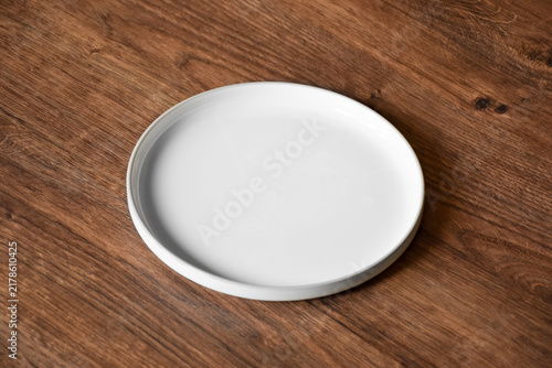 Ceramic white flat plate for food on wooden table top view