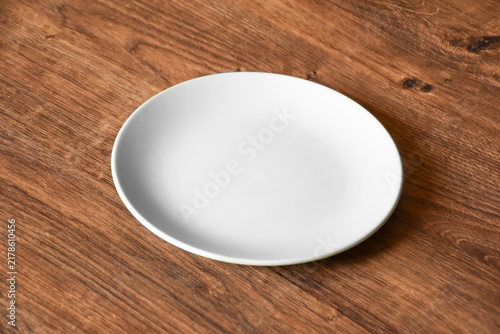 Ceramic white flat plate for food on wooden table top view