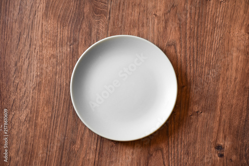 Ceramic white flat plate for food on wooden table top view