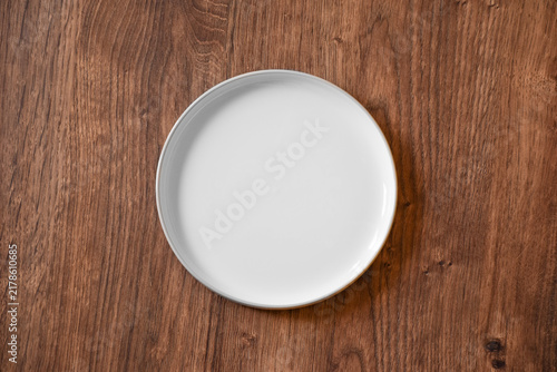 Ceramic white flat plate for food on wooden table top view