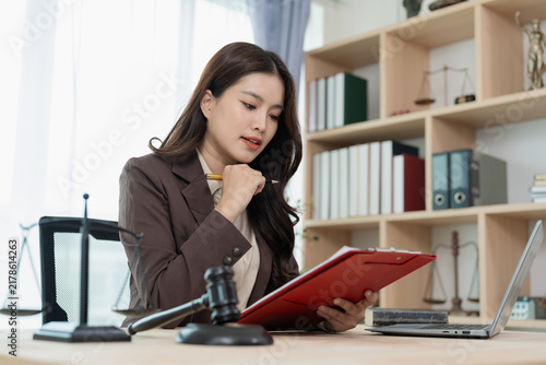Professional female attorney sitting at desk knocking gavel while working on legal documents and laptop in office.