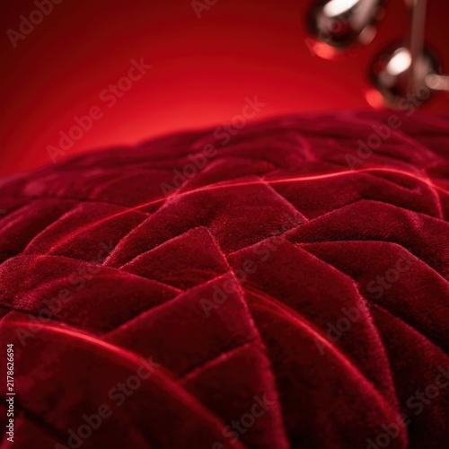 Close up of red velvet texture with woven pattern on cozy blanket. Soft plush fabric background in warm light. Luxury textile material for interior design and winter comfort concept.