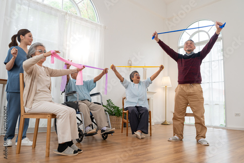 Caregiver leading senior group exercise with resistance bands in nursing home. Group of active Asian Elderly people stretching with elastic bands exercising in living room
