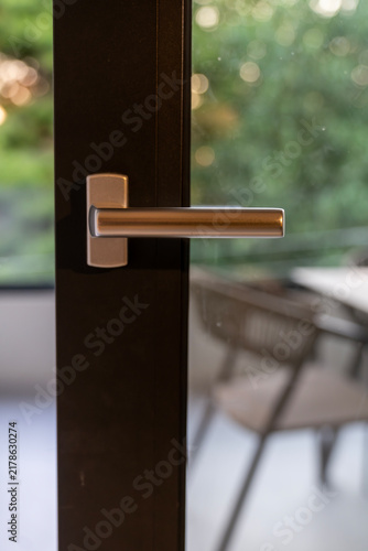 Close-up of modern silver handle on dark metal frame glass door with blurred garden background
