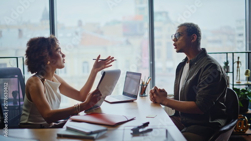 Фотография Colleagues discussing project in office meeting, woman presenting papers to man