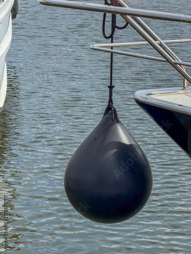 Black Teardrop Boat Fender Hanging from Yacht Railing at Marina