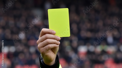 A close-up photograph of a hand holding a yellow card in a professional sports match during a competitive game