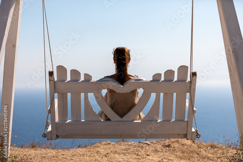Cuadro en lienzo A brown-haired woman sits on a white wooden bench with a heart-shaped pattern high above the sea