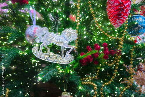 Christmas tree adorned with various decorations including a silver rocking horse ornament, red berries, gold bead garlands, and a large red pinecone-shaped bauble. Twinkling lights illuminate the gree