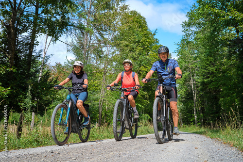 Three senior friends enjoy a cycling tour through a peaceful forest on a sunny day, promoting friendship, fitness and active aging in Naturpark Schönbuch, Herrenberg, Baden-Württemberg, Germany.