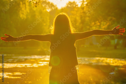 Young girl standing with open arms in warm golden sunlight, embracing the beauty of nature and symbolizing freedom, hope, happiness, inner peace and a positive new beginning. Horizontal image