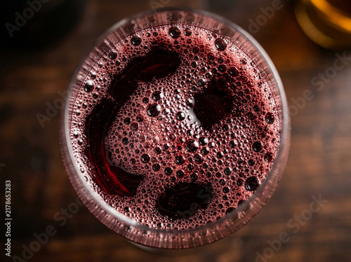 Top view of a glass of red wine with bubbles on the surface on a rustic dark wooden table background
