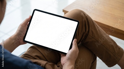 Person holding a digital tablet with a blank white screen while sitting in a bright indoor room with technology