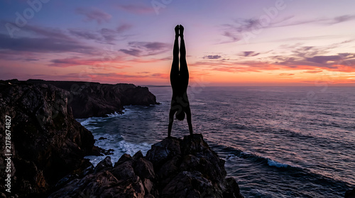 Obraz na płótnie Athletic silhouette performing a handstand on a rocky coastal precipice at dusk