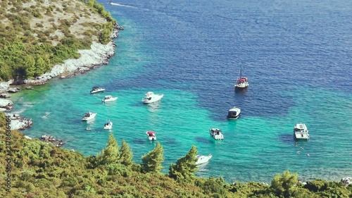 Aerial view of luxury yachts anchored in a turquoise bay surrounded by a rocky coastline and green forest. Summer seaside vacation scene. Drone view of the yachts.