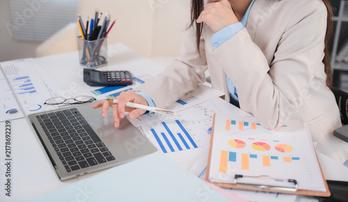 Obraz na płótnie Businesswoman Working in Office: A professional businesswoman diligently works at her desk, surrounded by financial reports, charts, and a calculator, engrossed in her tasks