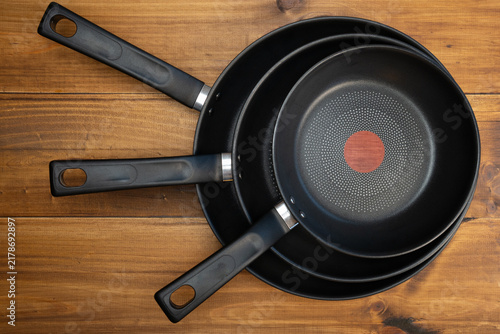 Foto Three black non-stick frying pans stacked on a rustic wooden kitchen table, top