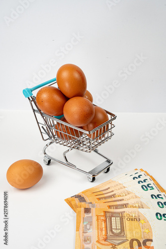 Принти на полотні Eggs filling a shopping cart next to Euro banknotes, representing increasing foo