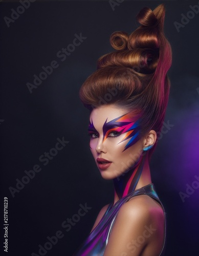 Woman posing with creative avant-garde hairstyle, futuristic body art makeup, and shimmering clothing, embodying beauty, fashion, and innovation against a dark background with subtle lighting
