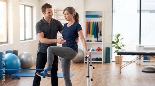 Fitness trainer helping a female client stretch her leg during a personal training session in a modern gym with copy space.