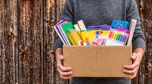 Donation box with school supplies and stationery on old wooden background held by volunteer