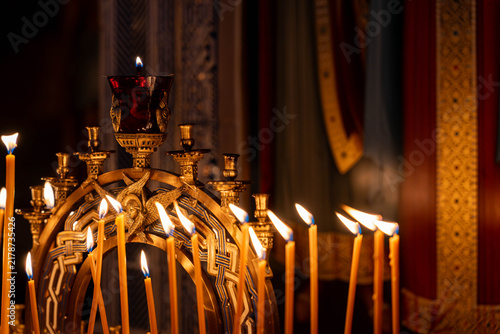 Foto Ornate altar candles burn inside dim sacred interior, with golden holder red glass lamp glowing above