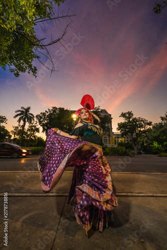 A sturdy Latina-Gypsy woman dancing traditional dances in the streets of Mérida, Yucatán, Mexico; the famous Regional Museum of Anthropology (Palacio Cantón) is visible in the background.
