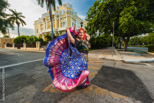 A sturdy Latina-Gypsy woman dancing traditional dances in the streets of Mérida, Yucatán, Mexico; the famous Regional Museum of Anthropology (Palacio Cantón) is visible in the background.
