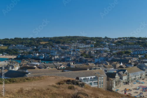 Canvastavla A wide, sunlit view of a coastal town with a harbor, numerous buildings, and a b