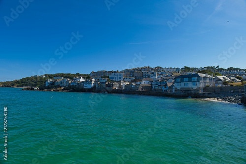 Фотография A vibrant coastal scene of St Ives, Cornwall, with numerous buildings lining the clear turquoise waters under a bright blue sky