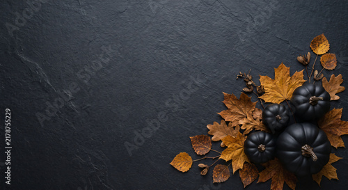 Top down flat lay of matte black pumpkins and autumn leaves with copy space