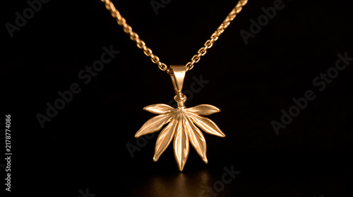 Elegant gold necklace with a detailed cannabis leaf pendant, known scientifically as Cannabis sativa, isolated against a dark background